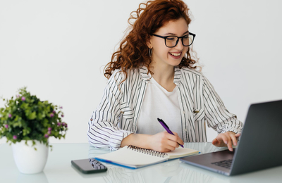 Redhead Ewoman Accountant Analyzes Documents Uses Calculator Makes Report Uses Laptop Computer Sits White Desktop Wears Spectacles Beige Jumper Poses Against White Home Interior (1)